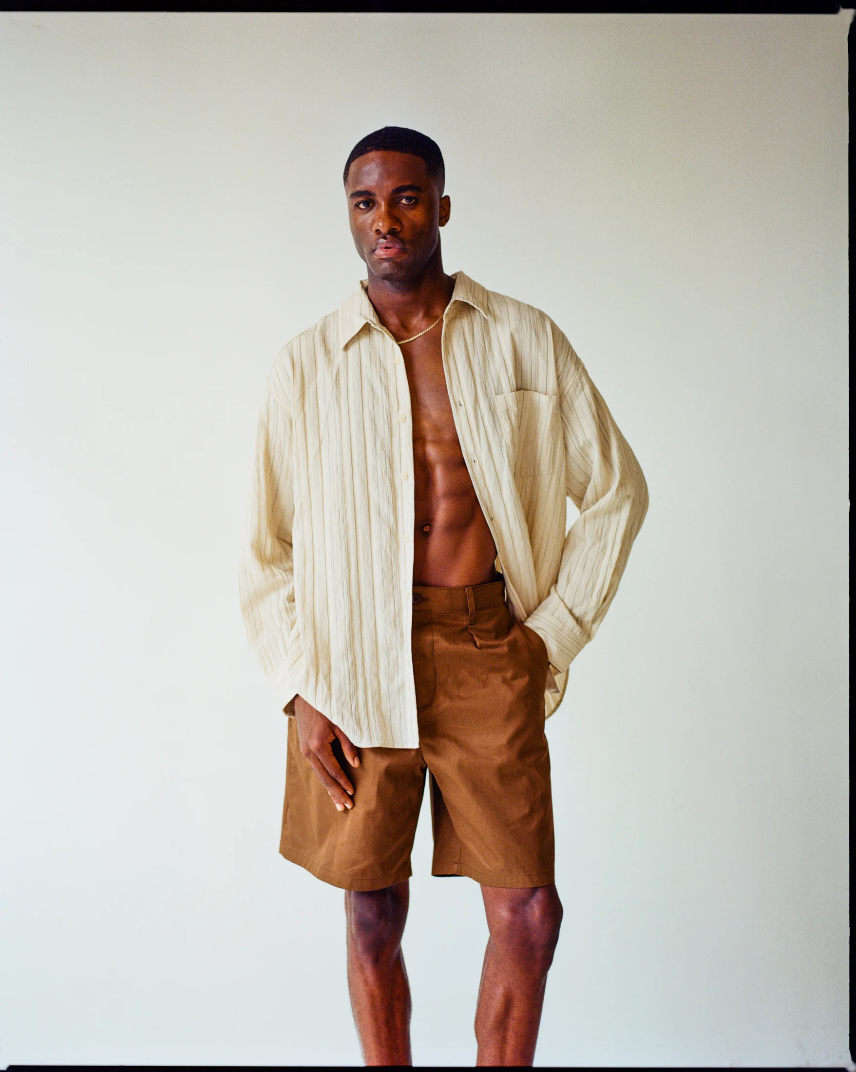 Rohan in a cream shirt and brown shorts, studio fashion portrait