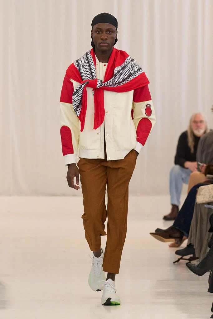 Rohan walking the runway in a cream jacket and red scarf